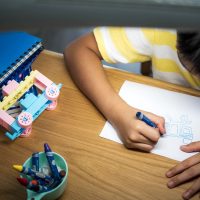 Boy sitting at the chair at table draws on the paper in bedroom.